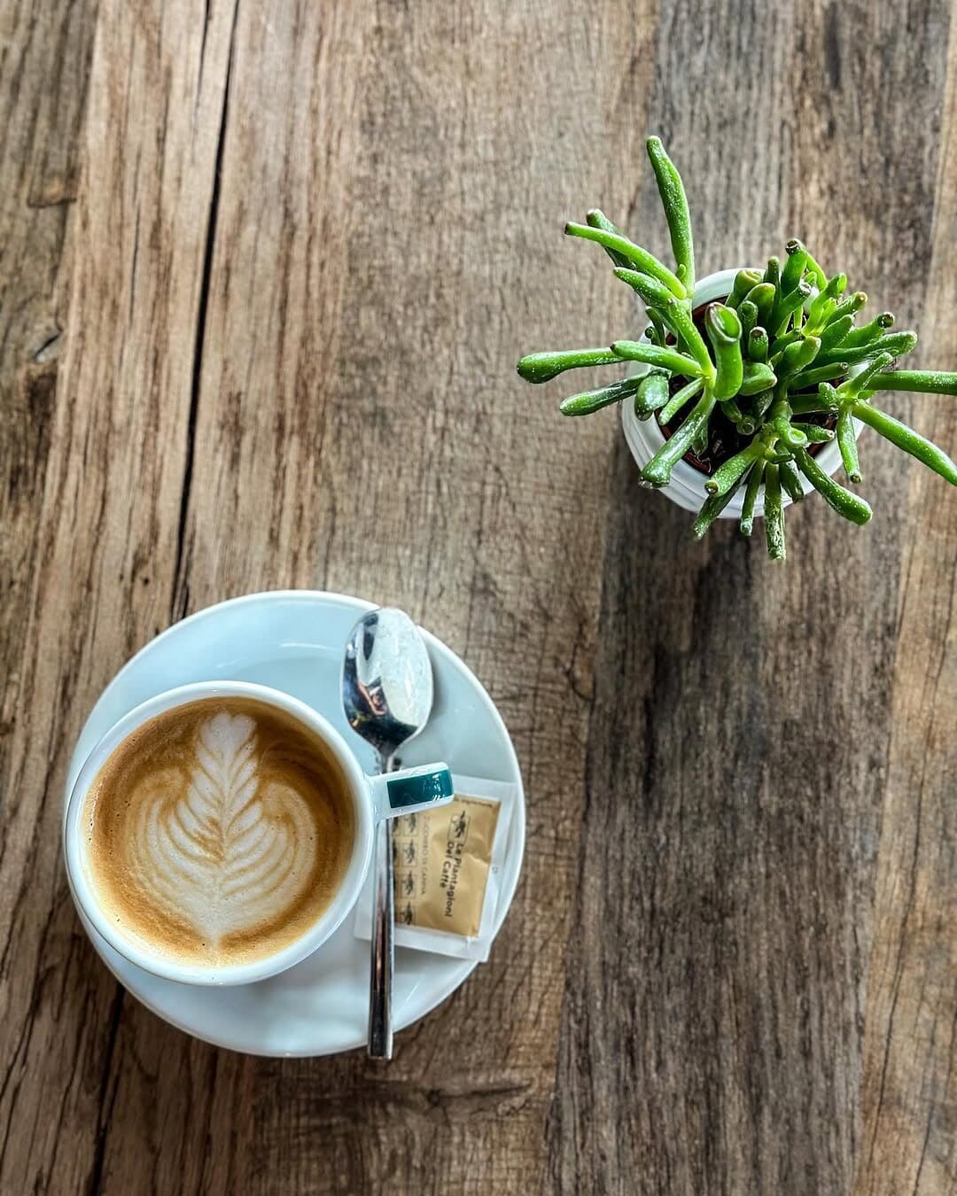 Cappuccino cu desen în spumă, pe o masă din lemn.