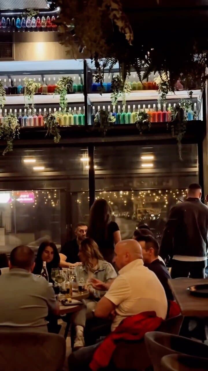 Bistroul seara, plin de oameni, cu barul luminat în spate.